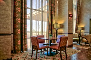 A hotel dining area with a table and chairs, patterned curtains, and a view through large windows.