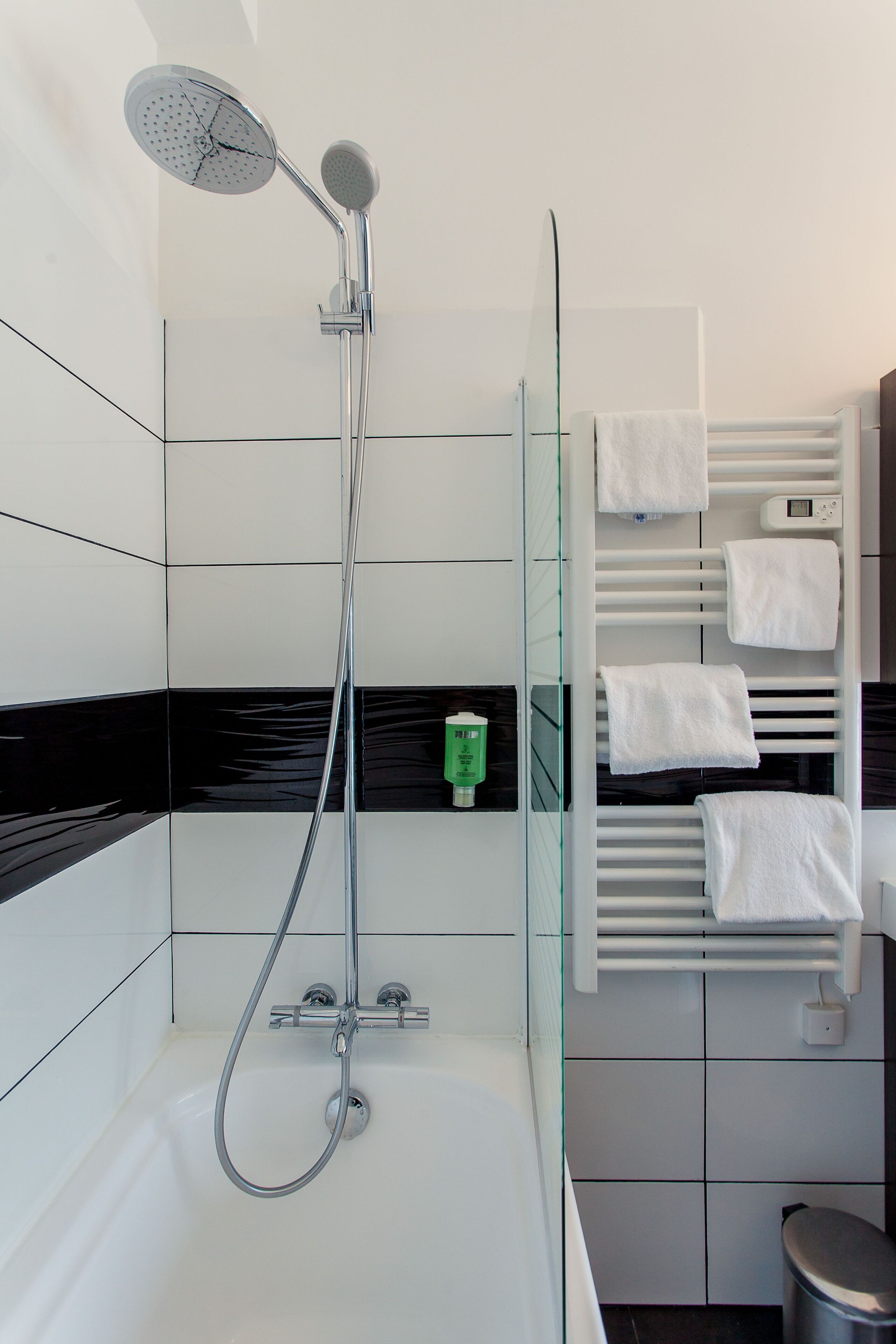 A modern bathroom with a glass-enclosed shower, white tiled walls, and a white towel rack with multiple towels.