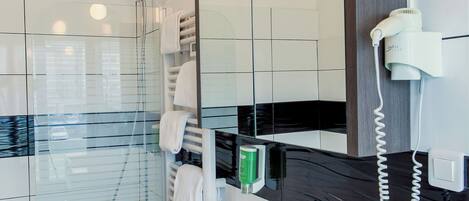 Un baño moderno con ducha envuelta en vidrio, un lavabo blanco, un espejo grande y un secador de pelo en la pared.