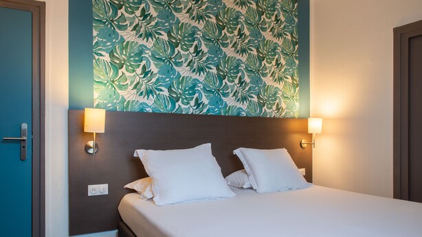 Una habitación de hotel con una cama, dos lámparas de noche, una pared con un diseño de hojas y una puerta.