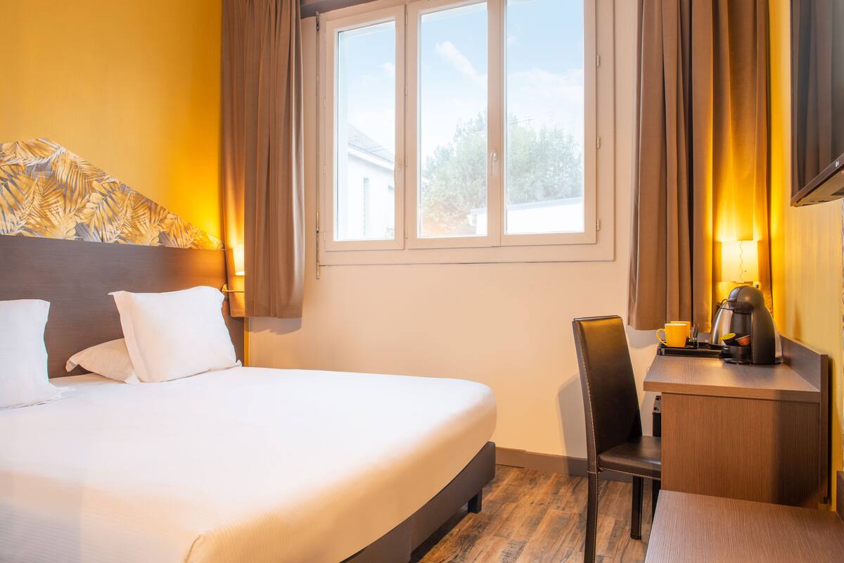 A hotel room with a bed, a desk, a chair, and a window with curtains.