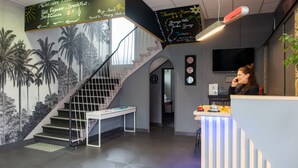 Un vestíbulo de hotel con una escalera, una recepción y una pared con murales de palmeras.