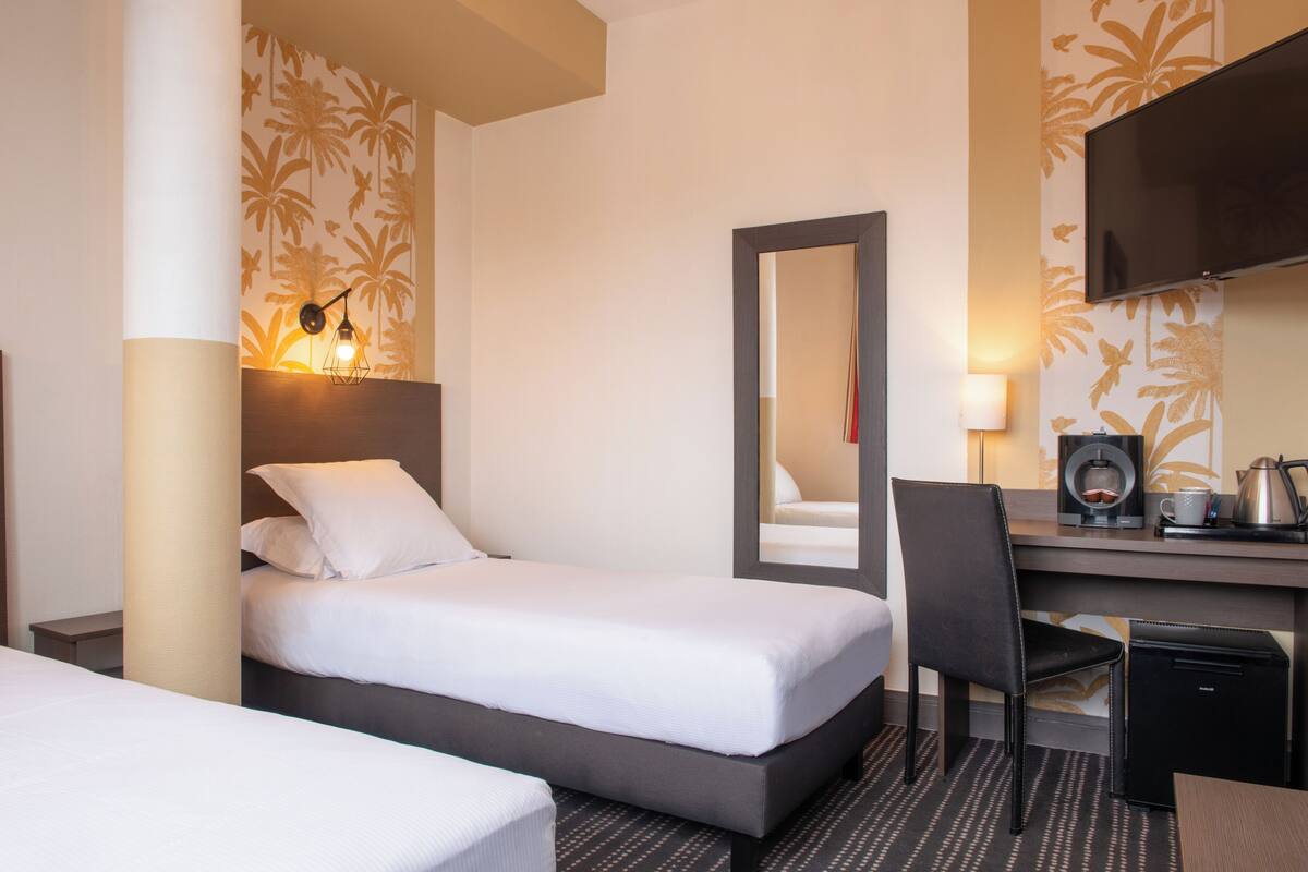 A hotel room with two beds, a desk with a chair, a flat-screen TV, a coffee maker, and a mirror.
