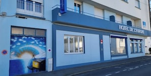 A hotel facade with a sign reading "HOTEL DE L'EUROPE," large windows, and a mural on the left wall.