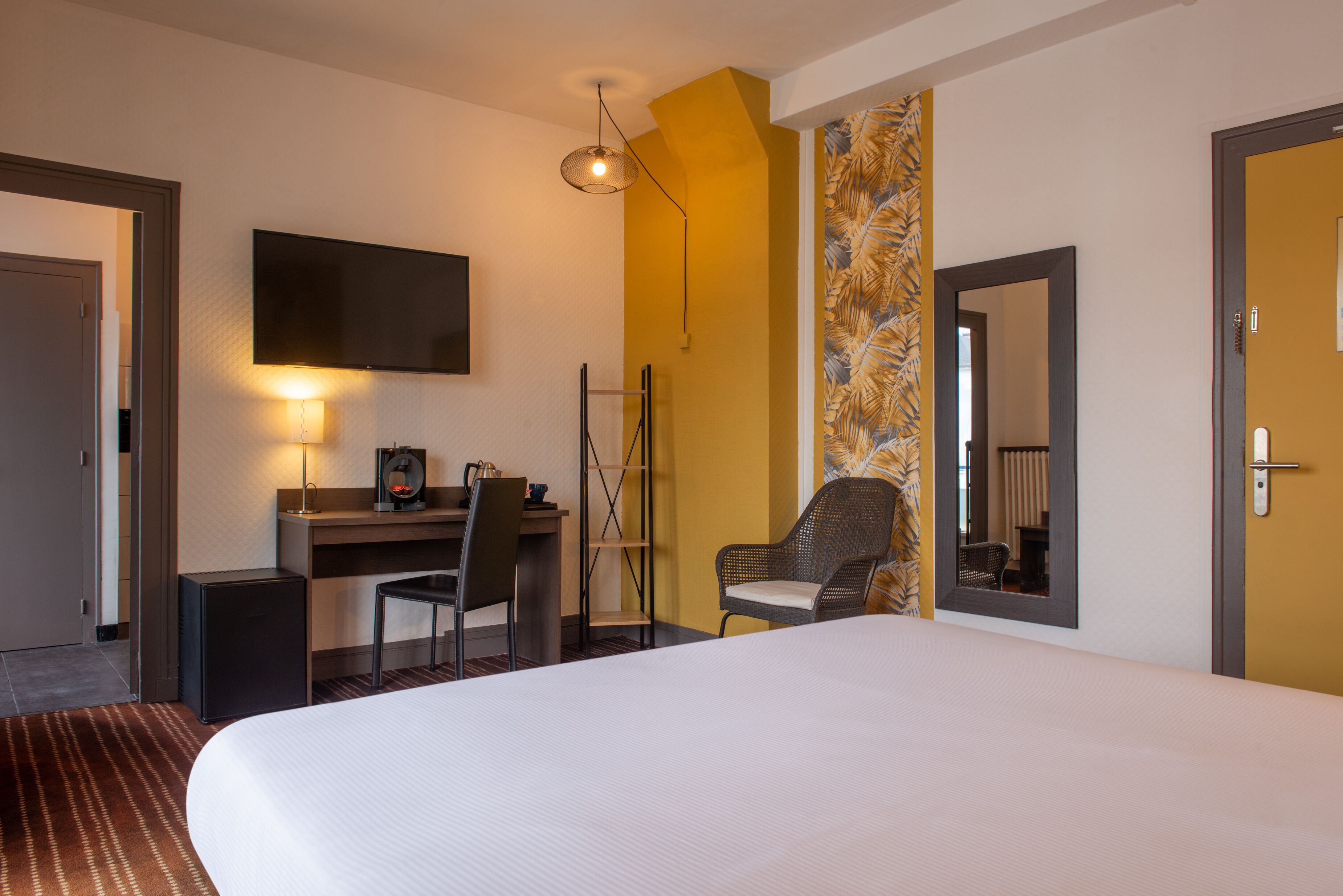 Une chambre d’hôtel équipée d’un lit, d’un bureau, d’une chaise, d’une télévision et d’un miroir.