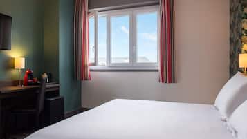 Habitación de hotel con una cama grande, un escritorio con silla, una cafetera y una ventana con cortinas.