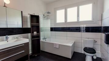 Un baño moderno con ducha de vidrio, lavamanos blanco y un inodoro negro.