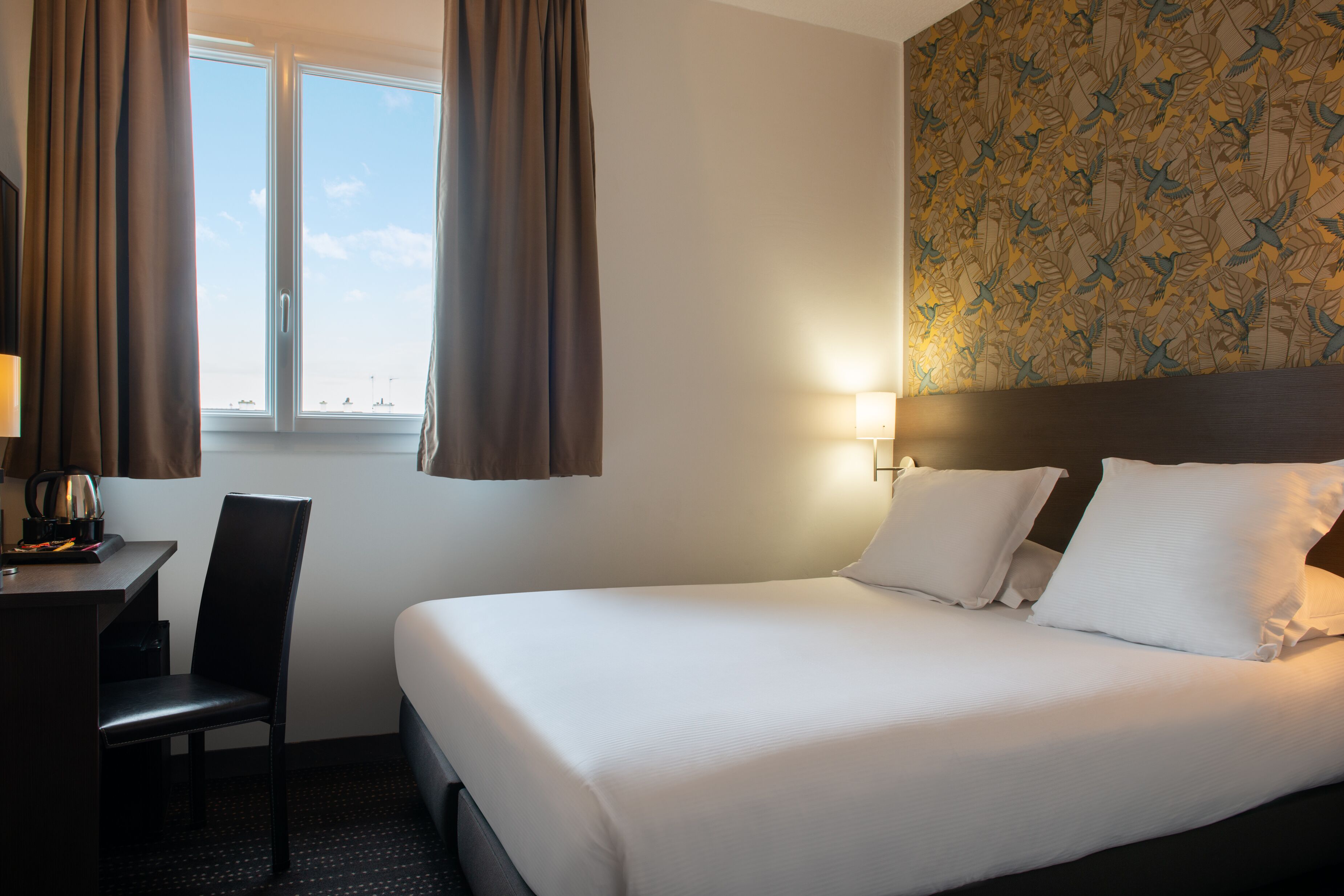 A hotel room with a bed, a desk, a chair, and a window with curtains.