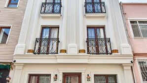 A two-story building with a central entrance, a balcony on the second floor, and a small outdoor seating area with two chairs and a table. - Kumru Hotel (Istanbul)