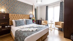 A hotel room with a large bed, a bedside table, a chair, a small table, and a window with curtains. - Kumru Hotel (Istanbul)