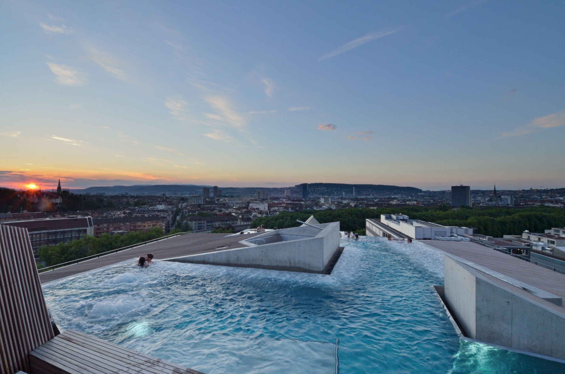 Piscina no terraço com vista para a paisagem urbana ao pôr do sol.