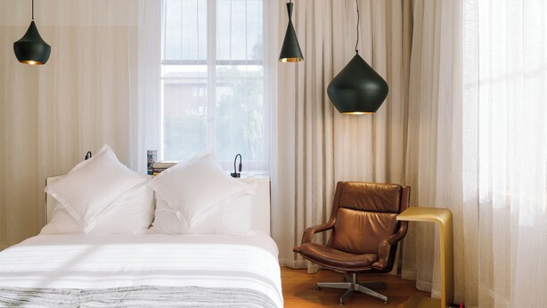 A bedroom with a bed, two hanging pendant lights, a leather chair, and a floor lamp. - B2 Hotel Zürich (Zürich)