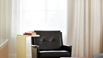 Een moderne kamer met een zwarte leren fauteuil, een klein tafeltje met boeken en een groot raam met dunne gordijnen.