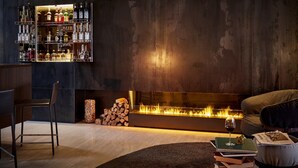 A modern living room with a fireplace, a bar area with liquor bottles, and a cozy seating arrangement. - B2 Hotel Zürich (Zürich)