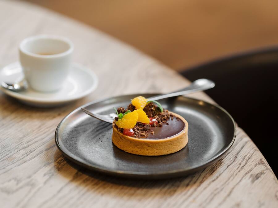 Dessert auf einem Teller mit Löffel, Tasse und Untertasse auf einem Holztisch.