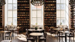 A library with bookshelves, tables, chairs, and large windows. - B2 Hotel Zürich (Zürich)