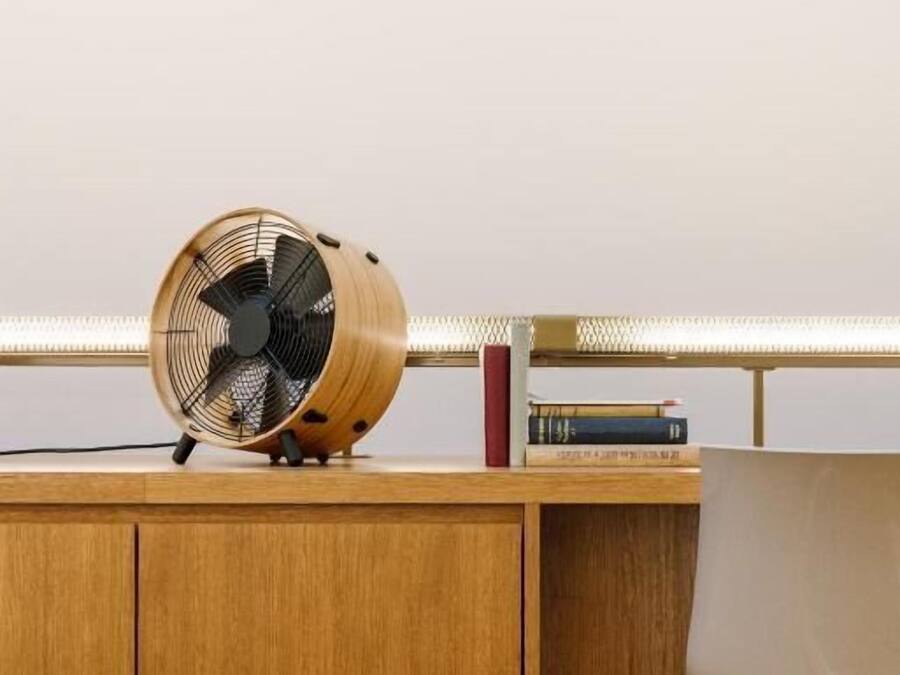 A wooden desk with a fan, books, and a chair.