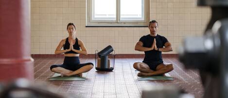 Two people sitting on yoga mats in a room with a tiled floor and a window.