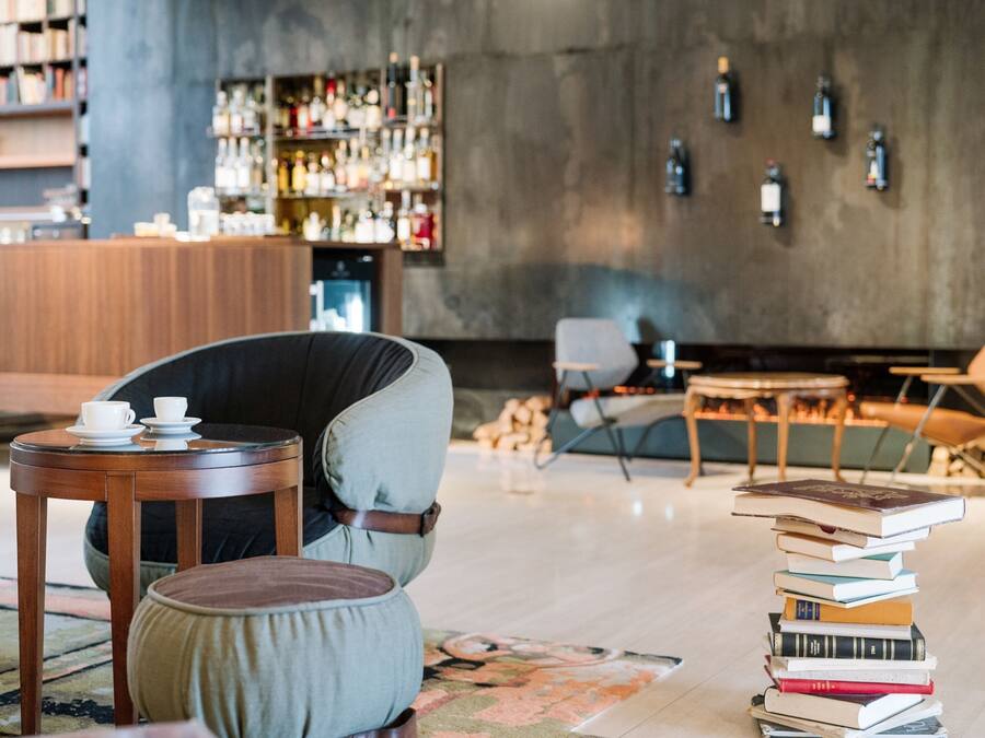 Uma área de estar moderna com uma mesa de madeira, uma poltrona estofada e uma pilha de livros.