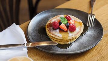 A breakfast setting with pancakes topped with berries and a cup of coffee on a wooden table.