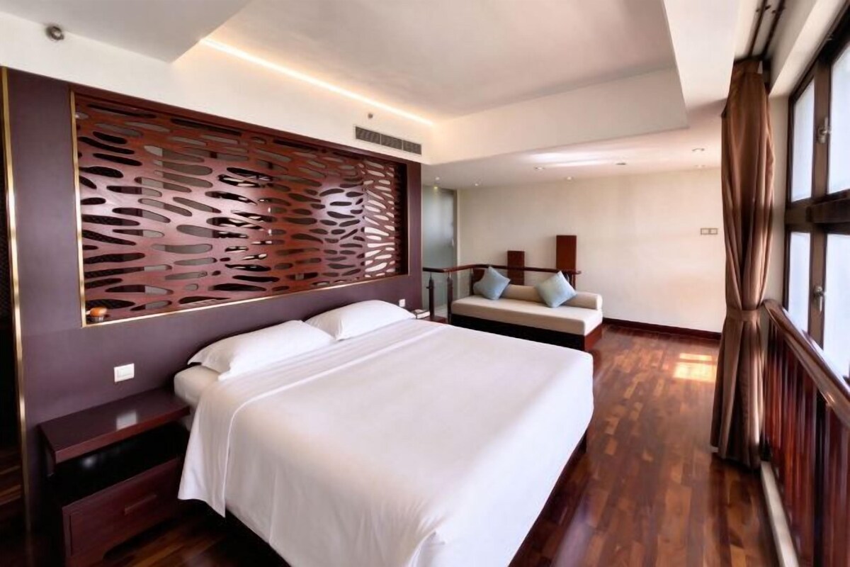 A hotel room with a large bed, a wooden headboard, a seating area with cushions, and a view of the outdoors.
