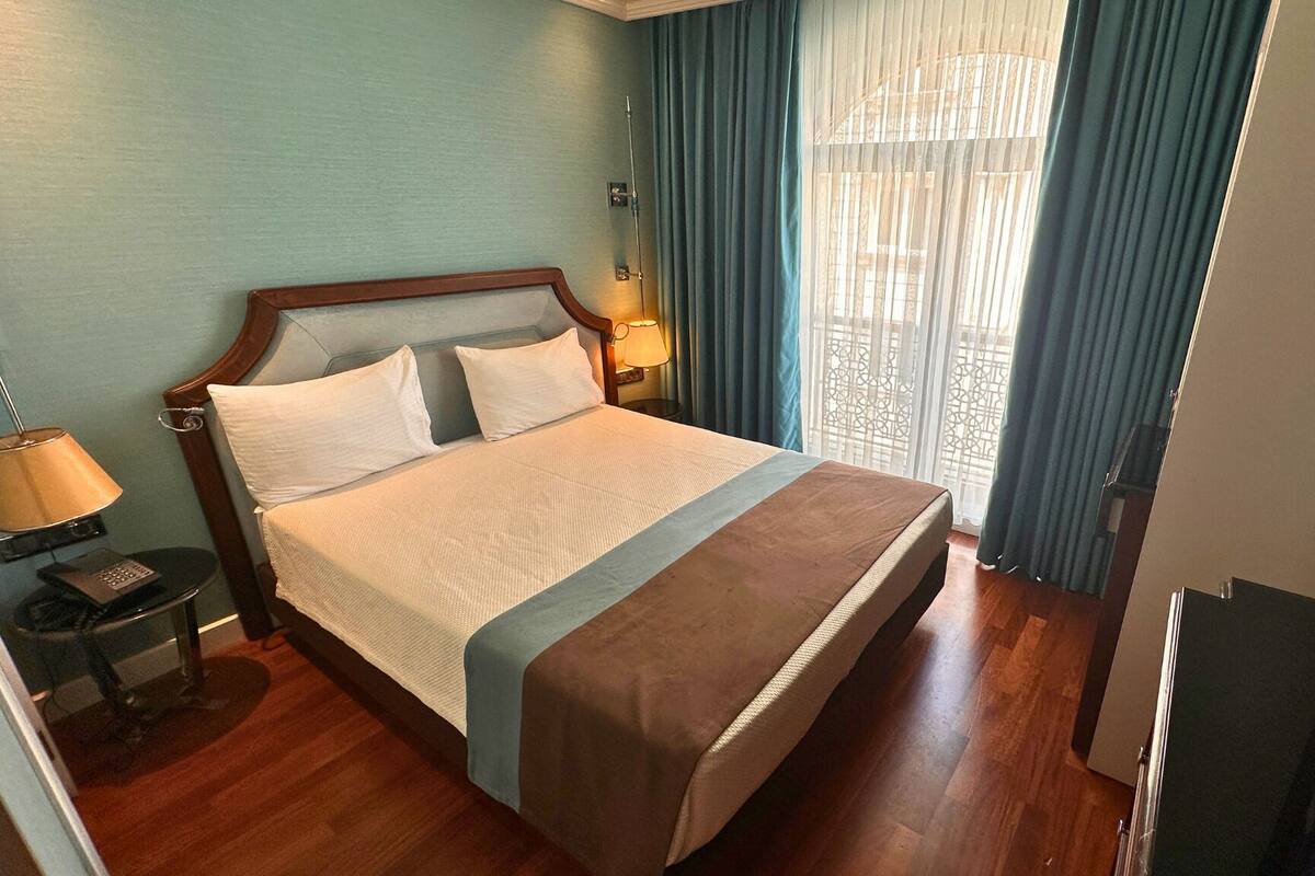 A hotel room with a bed, a bedside lamp, a TV, and a window with curtains.