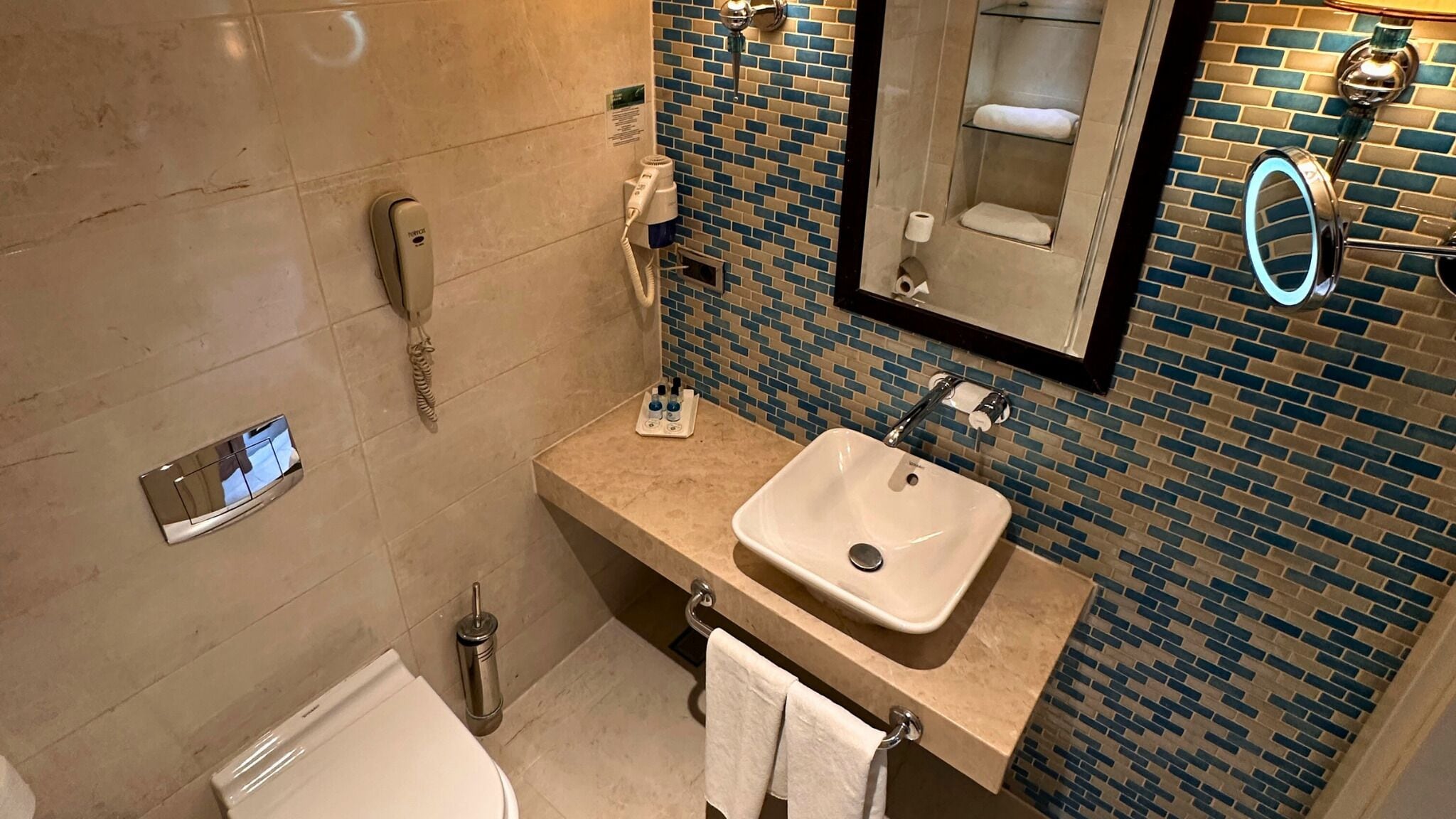 A bathroom with a white sink, a mirror, a towel rack, a hairdryer, and a phone.