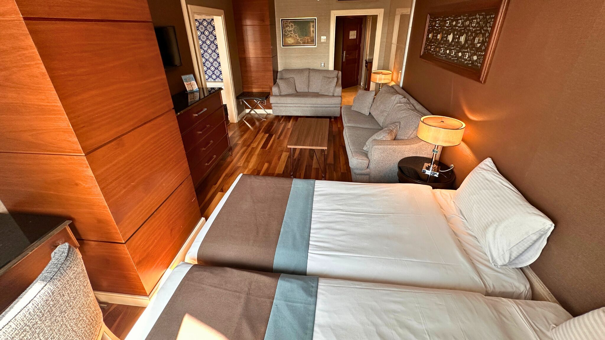 A hotel room with a bed, a sofa, a small table, and a lamp.