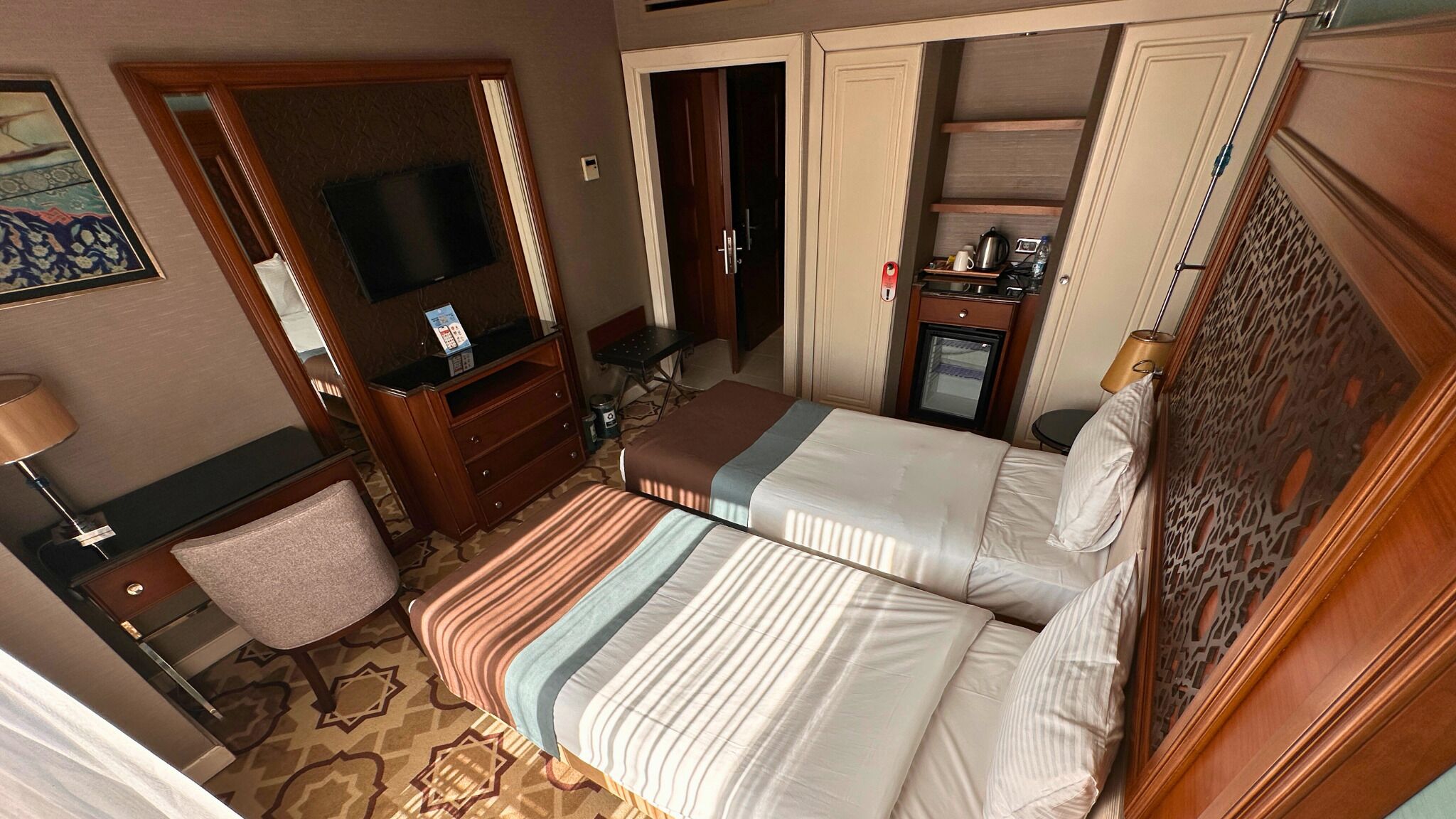 A hotel room with two beds, a TV, a desk, and a minibar.