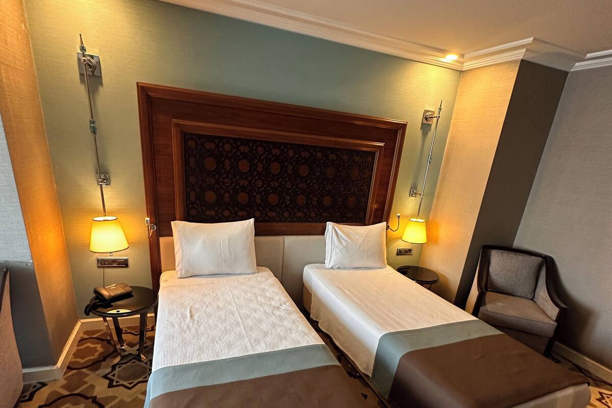A hotel room with two beds, a wooden headboard, patterned carpet, and bedside lamps.