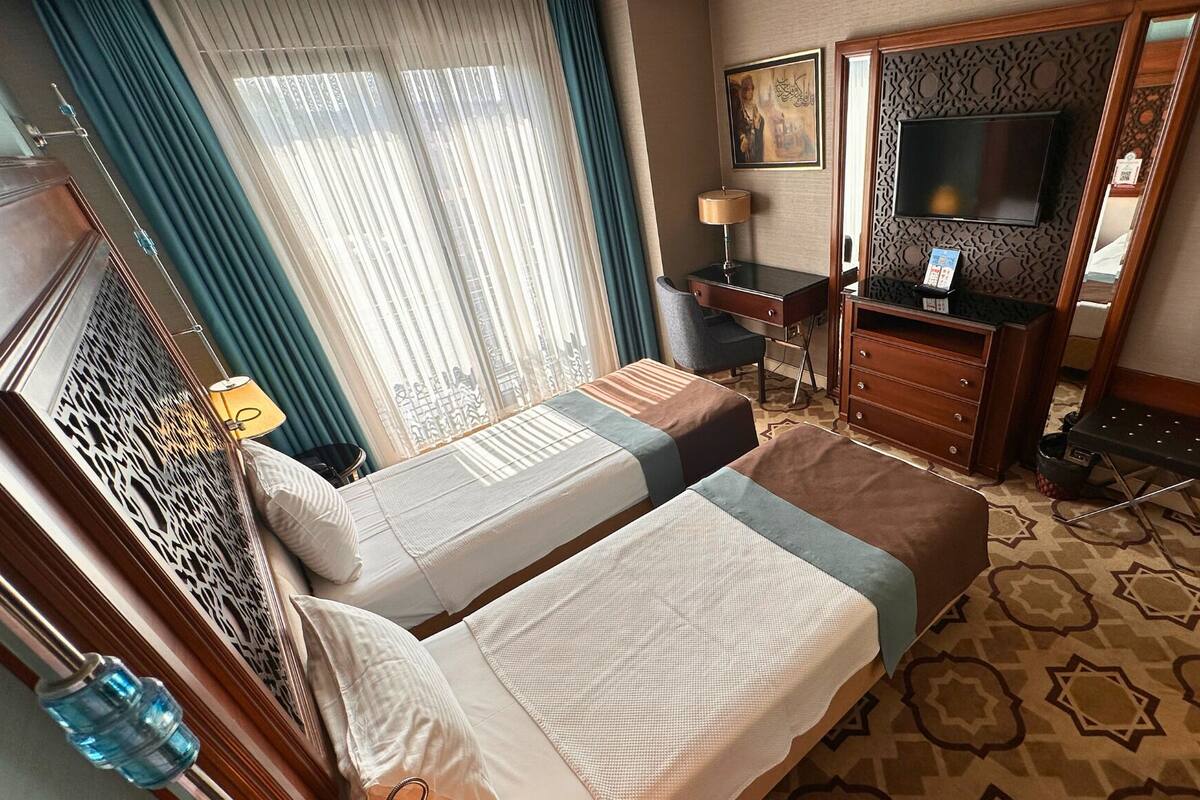 A hotel room with two beds, a desk, a TV, and a patterned carpet.