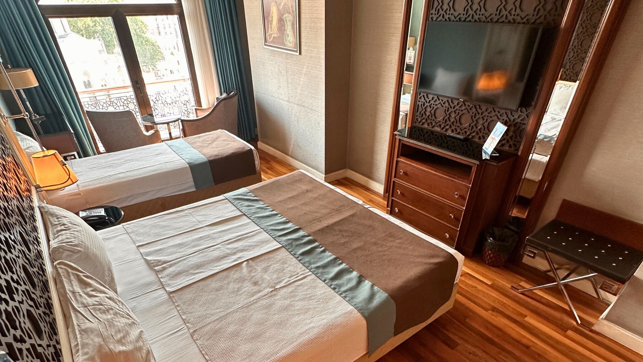 Habitación de hotel con dos camas, un aparador, un televisor y una ventana con vistas a edificios.