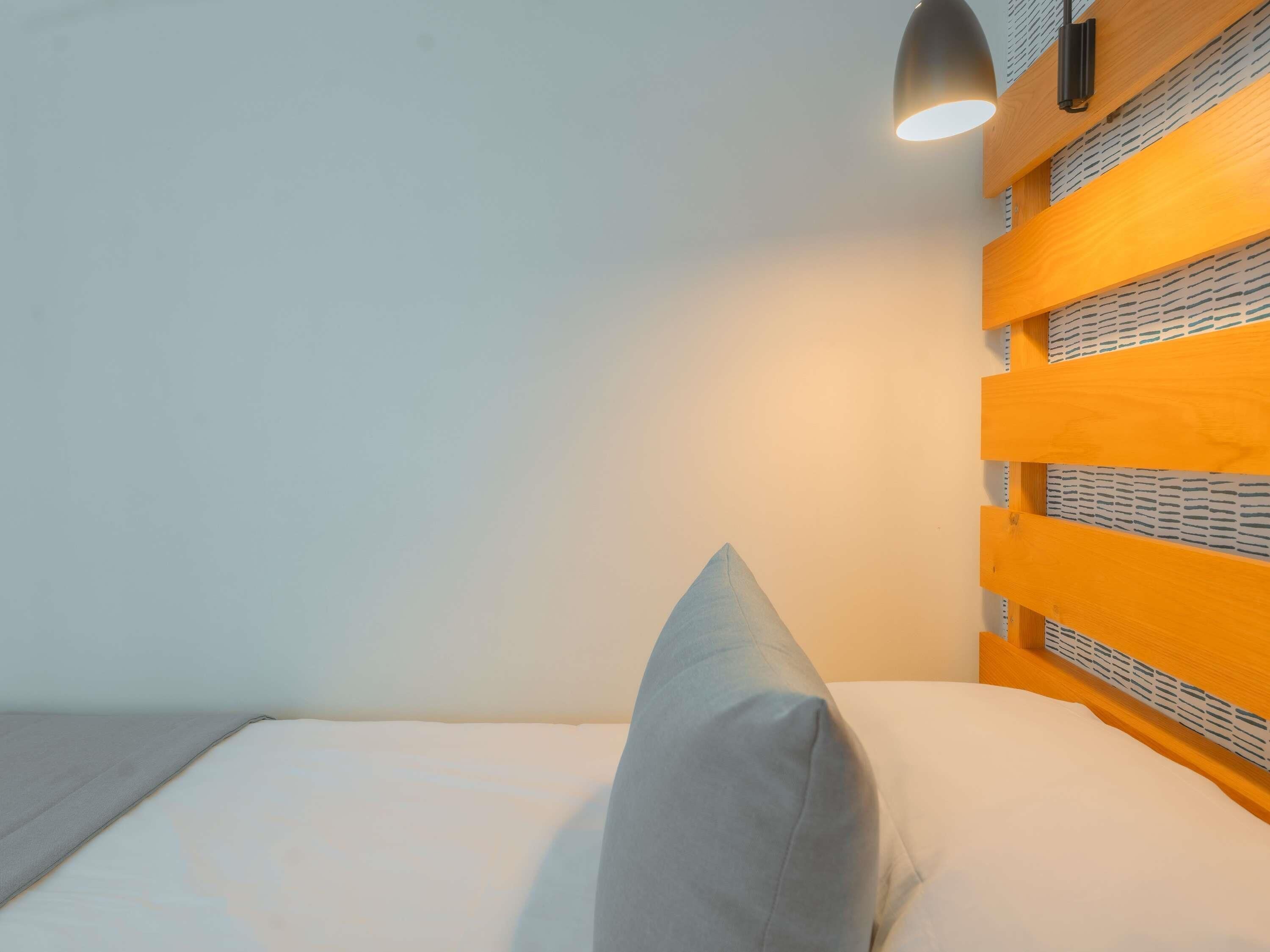Una cama con almohada, cabecera con diseño estampado y lámpara colgante.