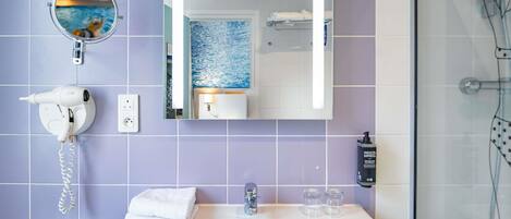 A bathroom with a white sink, a mirror, a hairdryer, a towel, and a shower.