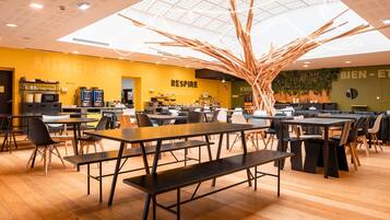A modern restaurant with wooden floors, black and white chairs, and a central wooden art installation.