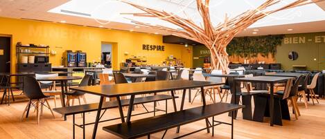 Um restaurante moderno com pisos de madeira, cadeiras pretas e brancas e uma instalação artística central de madeira.