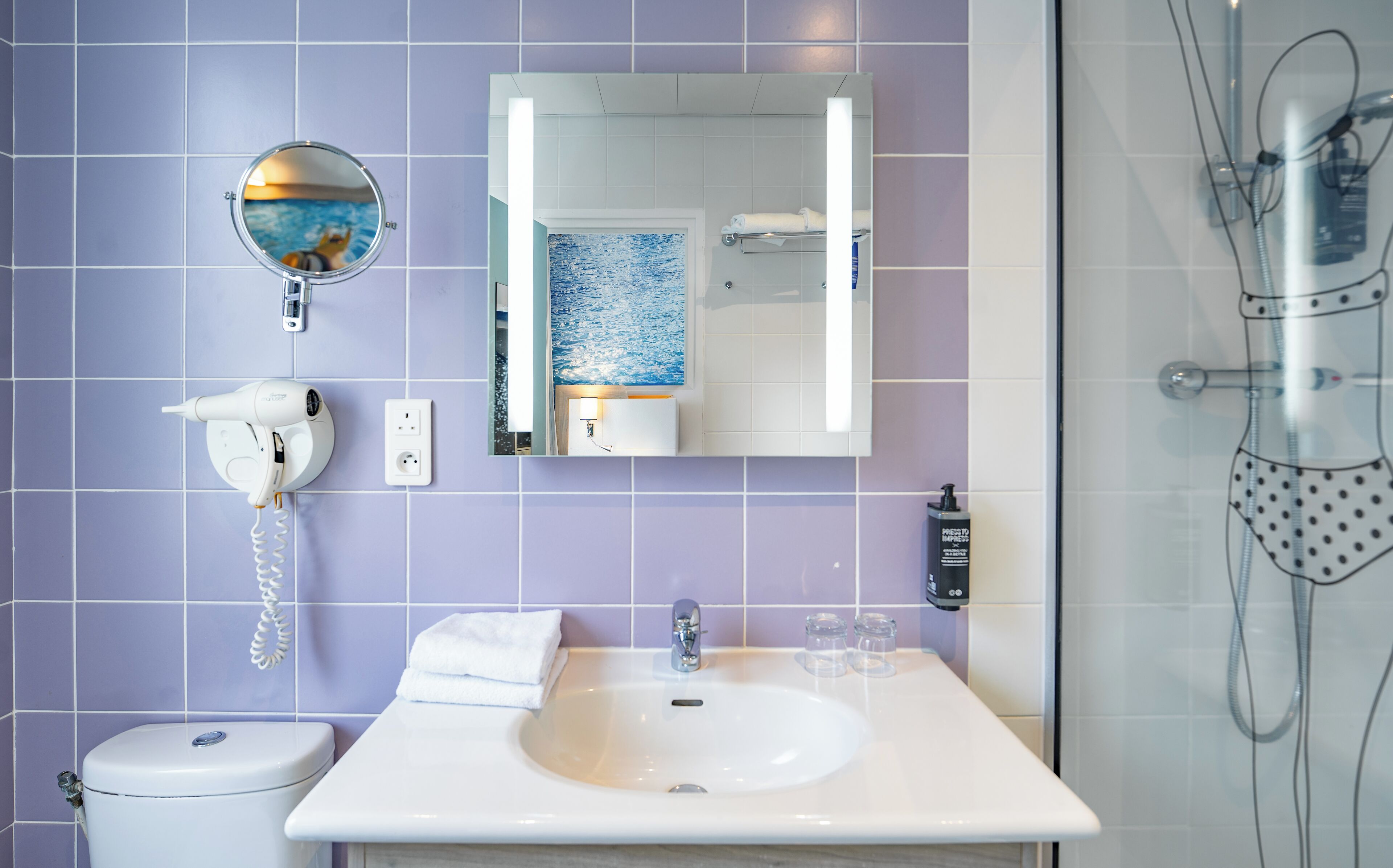 A bathroom with a white sink, a mirror, a hairdryer, and a shower.