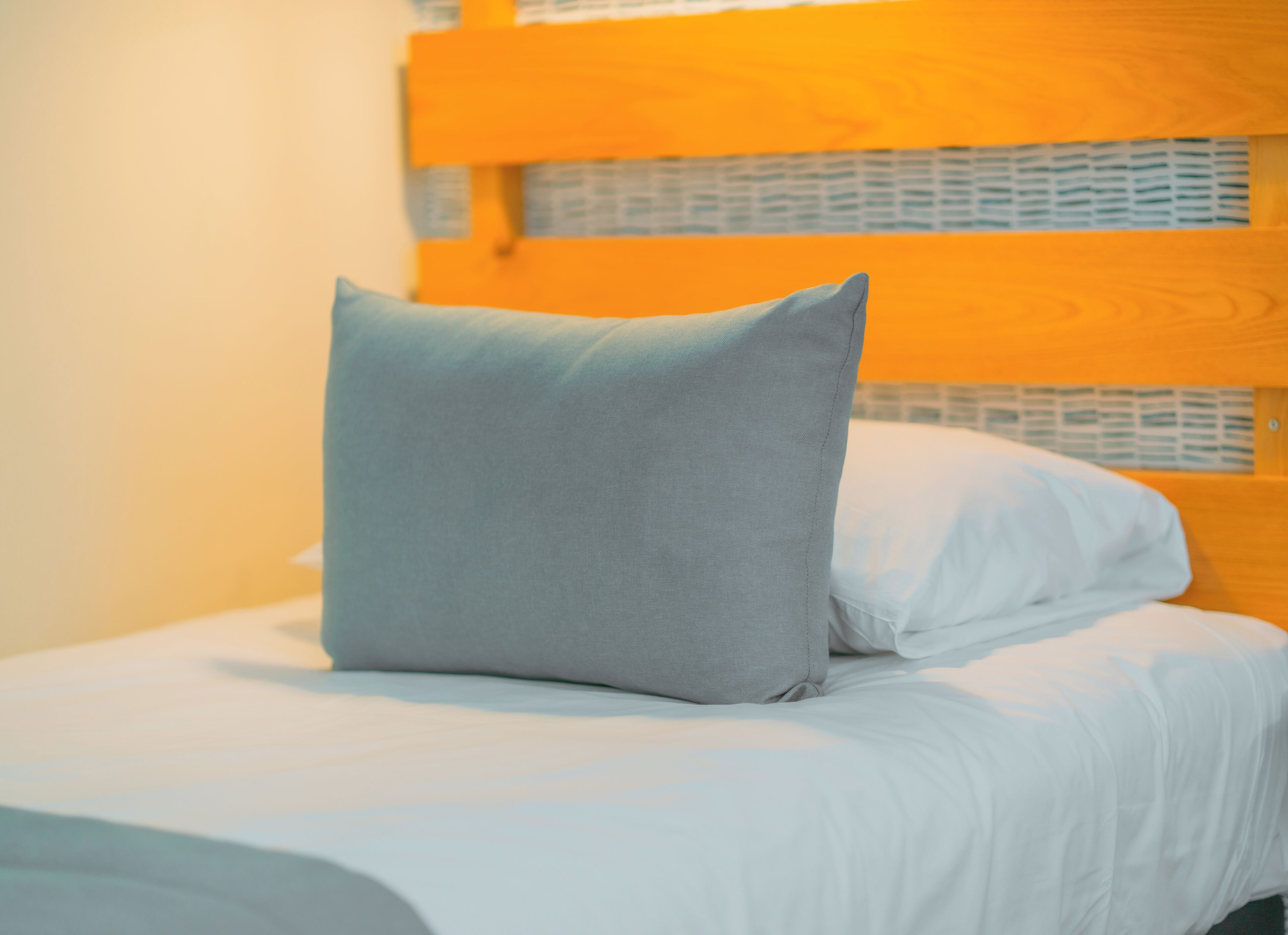 A bed with white bedding and a single grey pillow.