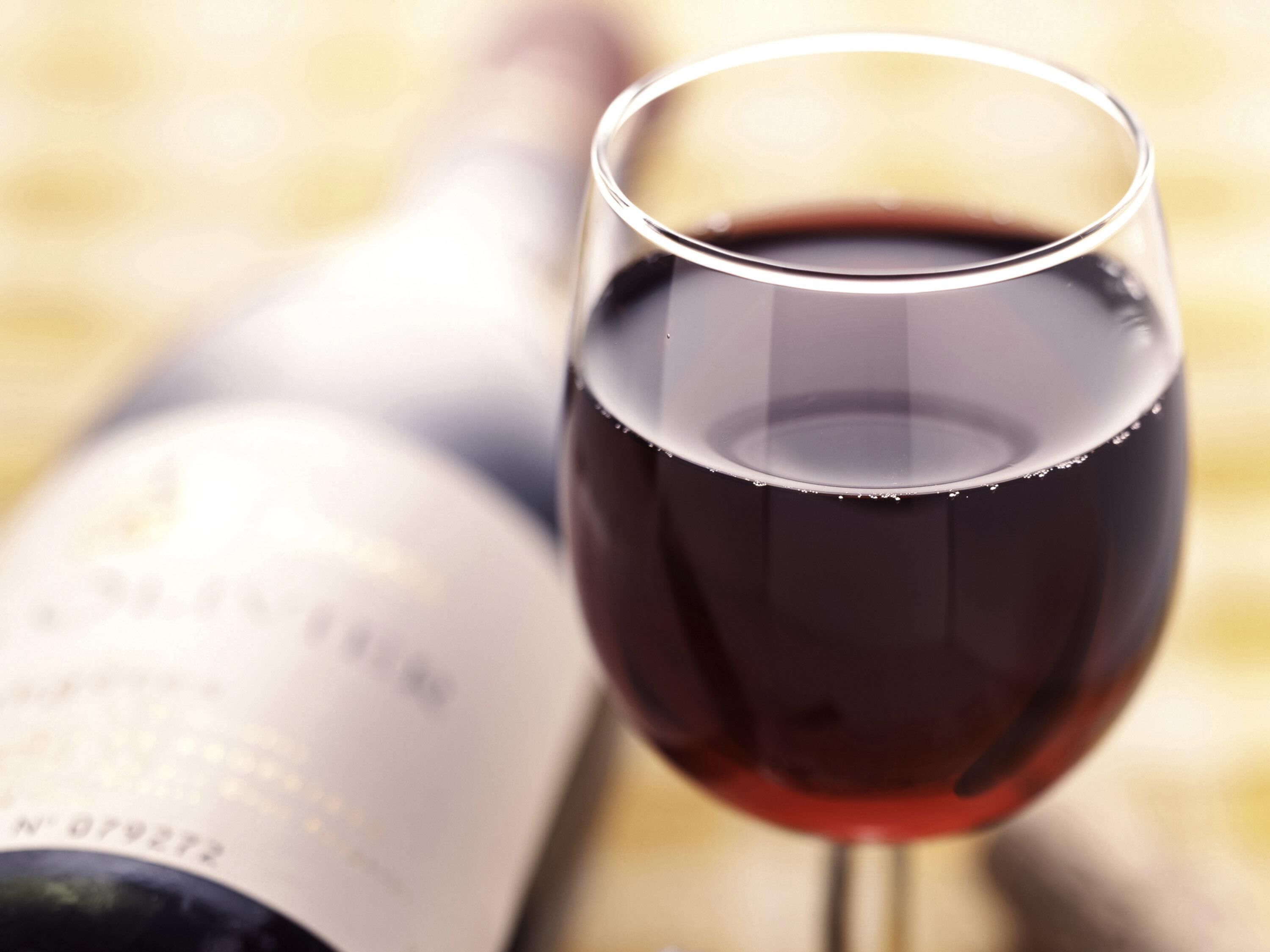 A wine glass filled with red wine and a blurred bottle in the background.