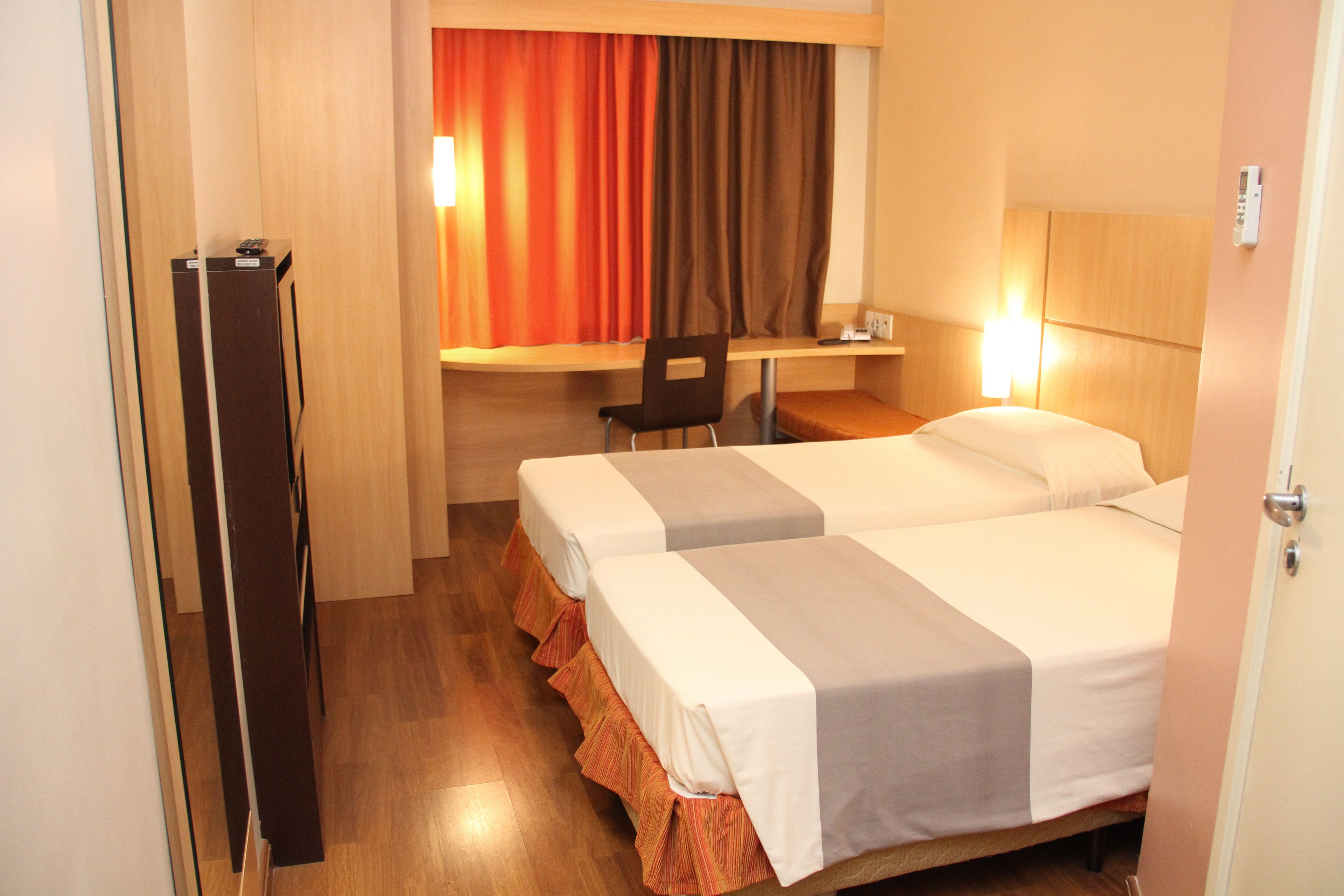 Quarto de hotel com duas camas, uma escrivaninha e uma cadeira.