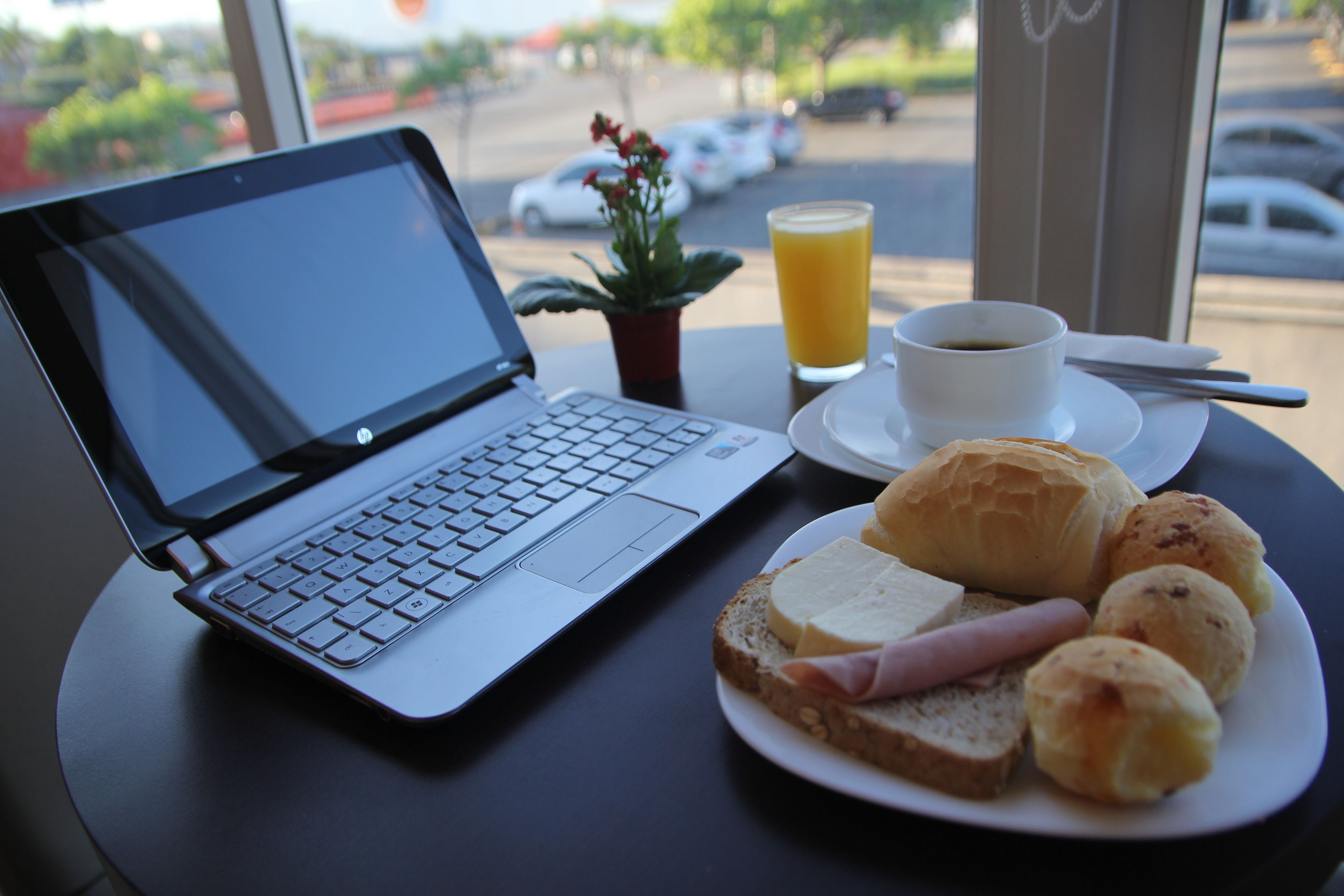 Una laptop sobre una mesa con un plato de comida, una taza de café y un vaso de jugo de naranja.