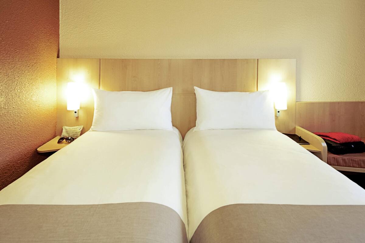 Habitación doble con dos camas, lámparas de noche y cabecera de madera.