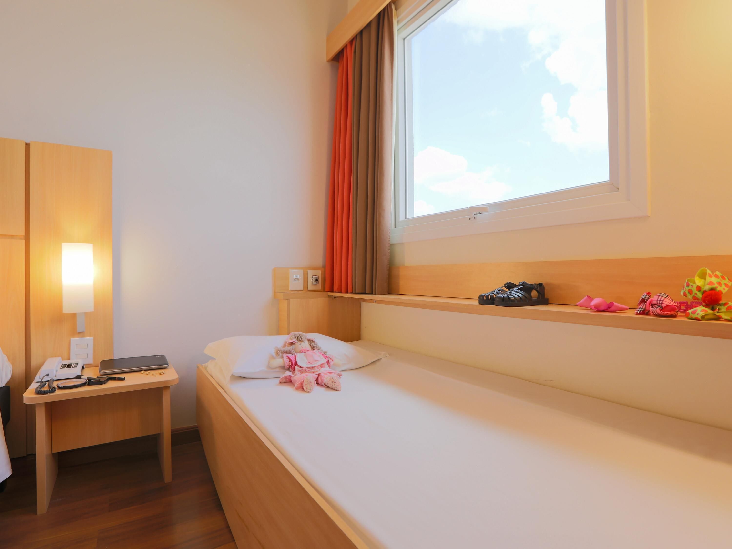 A hotel room with a bed, a bedside table with a lamp, a phone, and a laptop.