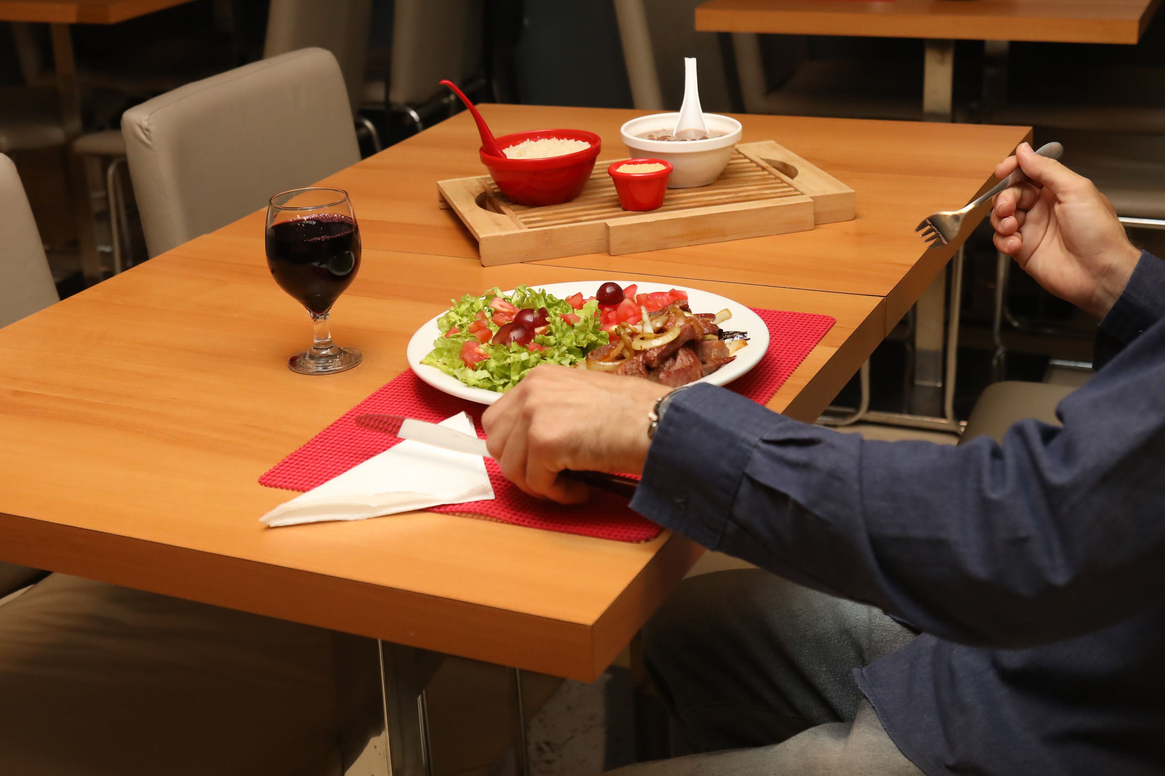 A dining table with a plate of food, a glass of red wine, and a red bowl with a spoon.