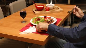 A dining table with a plate of food, a glass of red wine, and a red bowl with a spoon.