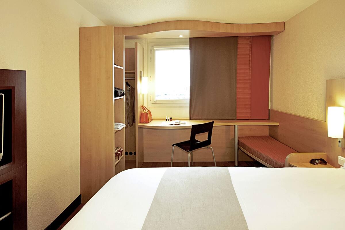 Habitación de hotel con cama, escritorio, silla, armario y ventana.
