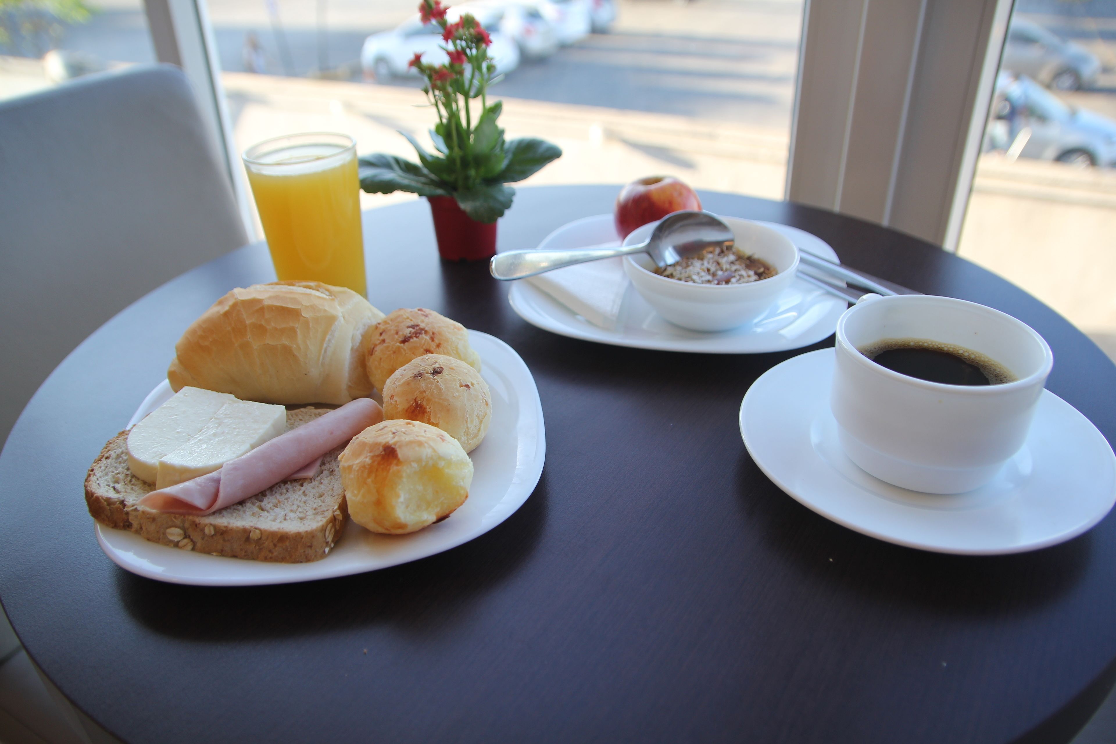 Una colazione con croissant, prosciutto e pane su un piatto, una ciotola di cereali, un bicchiere di succo d'arancia e una tazza di caffè su un tavolo.