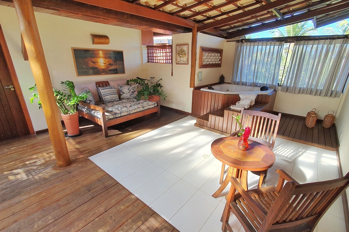 A wooden deck with a sofa, a small table with a vase, and a hot tub area.