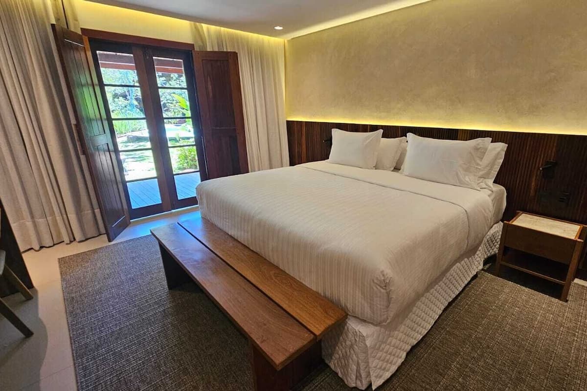 A large bed with a wooden headboard, a bench, and a bedside table with a lamp.