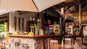 An outdoor bar area with stone walls, wooden furniture, and tropical decor. - Pousada Casa Do Forte (Mata de São João)